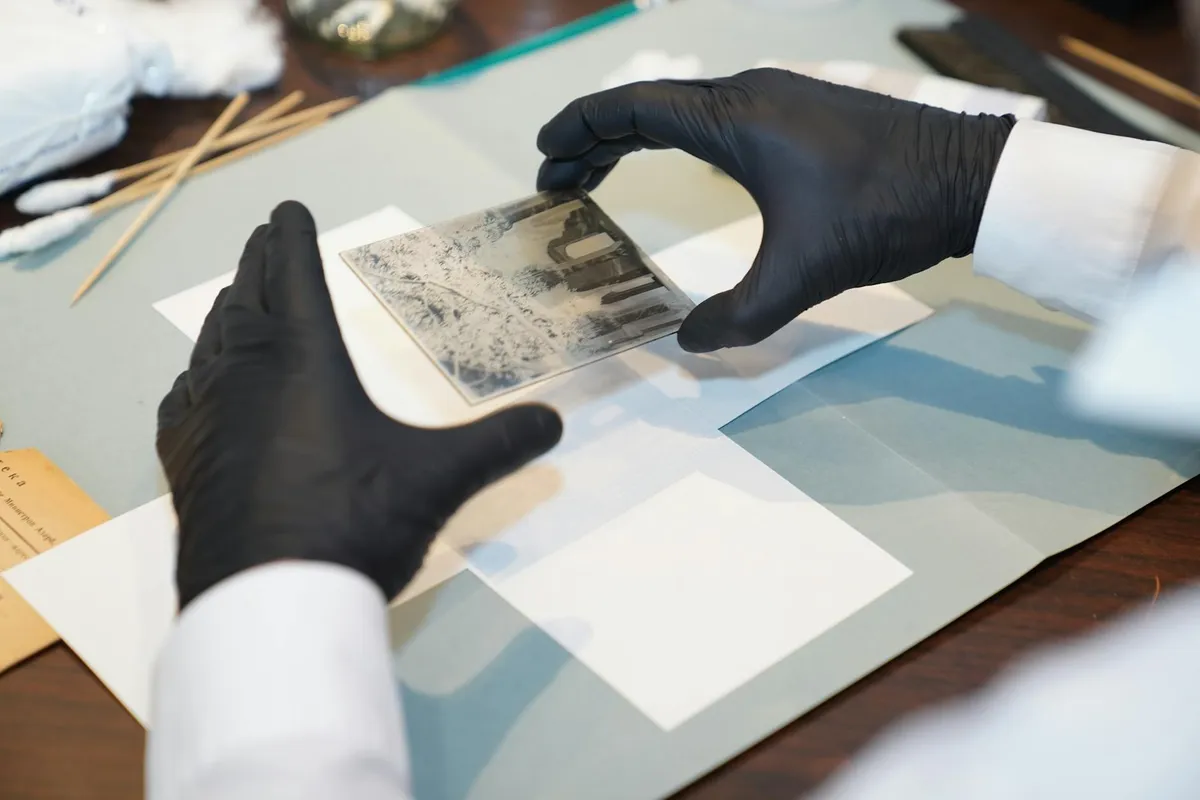 A conservator's gloved hands working on an archival surface under soft studio light